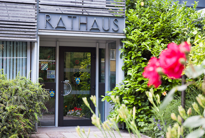 Bild des Haupteinganges zum Rathaus Poing mit Rosen im Vordergrund.